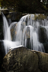 Flowing waterfall cascades over large rocks surrounded by shaded green vegetation, creating a peaceful scene associated with nature, relaxation and fresh water. © Инна Мадеева