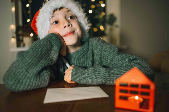 A boy in a Santa hat thinks about his Christmas letter