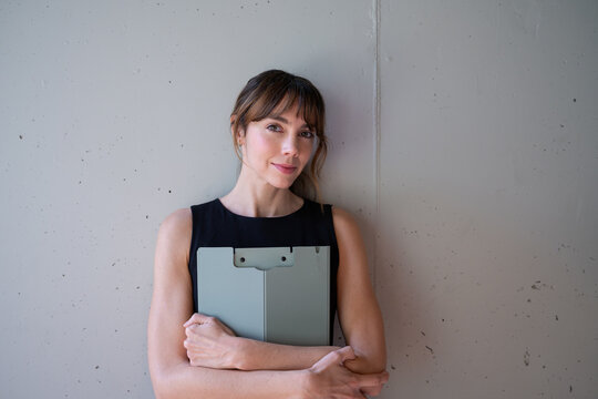 Confident businesswoman holding folder in front of concrete wall