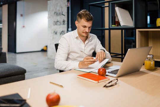 Businessman writes notes at office desk with laptop