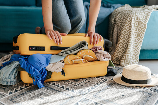 Hands press to close an overpacked yellow suitcase indoors