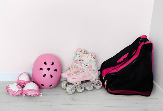 Pink kids roller skates, helmet, protective gear, and sports bag set against a light wall. Rollerblading and active kid leisure concept