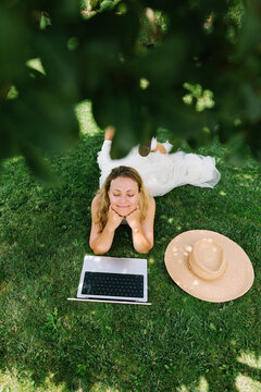 A smiling woman relaxes on grass with a laptop outside