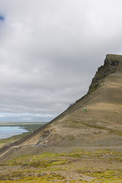 Steep rocky mountainside above the old road at Almannaskard, overlooking Hornafjordur coastal waters and lowlands under heavy cloud in southeast Iceland on a summer day.