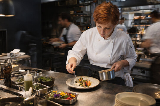 Female chef plating vegetables during busy restaurant service