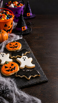 Halloween iced cookies with candy buckets on a dark wooden table