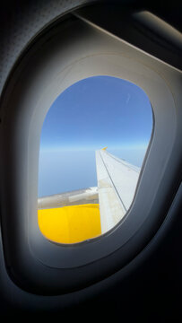 Passenger travel view from an aircraft cabin through an airplane window with the wing against a blue sky during flight and the wing framed by the window