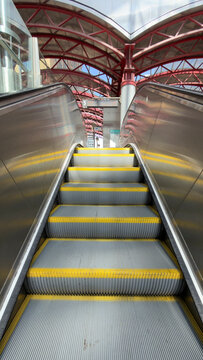 Modern interior with an escalator and yellow steps beneath a red steel and glass roof where symmetry follows the escalator toward the roof and steps