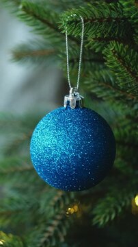 Vertical video. Person decorating Christmas tree with blue Christmas ornaments. 