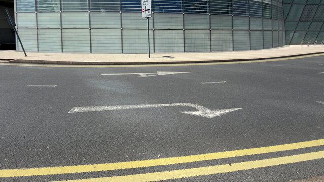 Empty urban street with a directional arrow and yellow lines beside a glass facade where the arrow and lines guide the view across the street