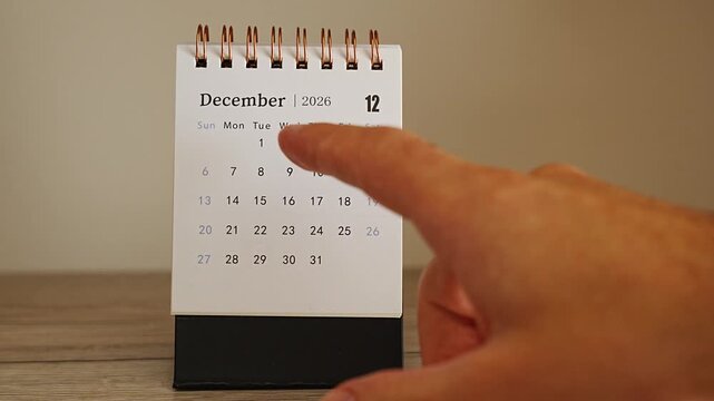 Blurred finger in the foreground reaching toward sharp dates on a desk calendar for December 2026, selective focus on the spiral bound page, concept of countdown, waiting and approaching deadlines