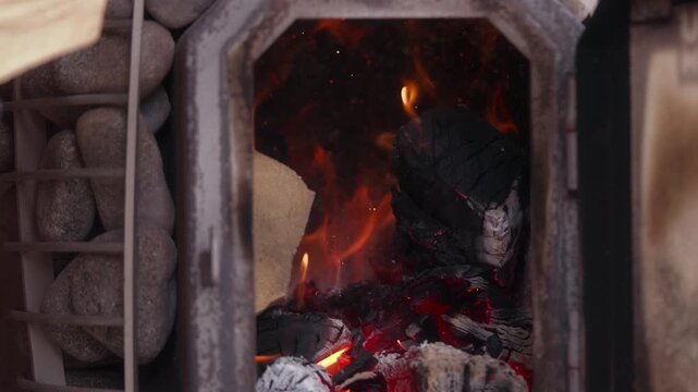 Gloved hand stokes embers in a stone sauna stove with fire