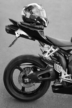 Naked sport bike tail section showing license plate with black motorcycle helmet hard hat on seat top, premium two wheeler vehicle Back rear wheel exhaust pipe brake disk chain frame street superbike