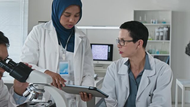 Diverse multiethnic scientists collaborating in laboratory with Asian young adult man examining sample under microscope. Clip suited for medical research, biotechnology and science education