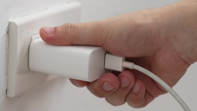 close up hand plugging adapter charge the battery with outlet socket plug and hold mobile phone on wall ,electric safety concept