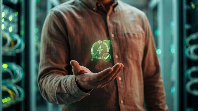 Green data center and sustainable energy technology concept, man holding holographic leaf with lightning bolt, recycle arrows and checkmark in server room for eco friendly IT
