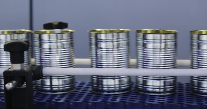 Open tin cans travel in organized clusters across blue modular conveyor. Precision guides control movement preparing containers for canned food product filling