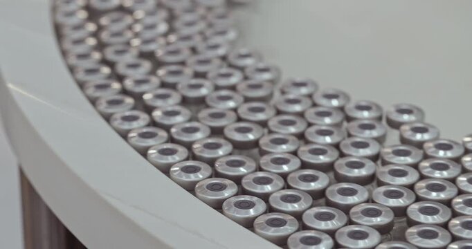 Vials with aluminum caps move in organized rows through automated pharmaceutical production line. Precision handling supports efficient packaging workflows