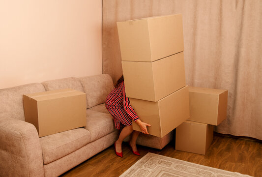 Woman in dress struggles carrying heavy cardboard box stack indoors