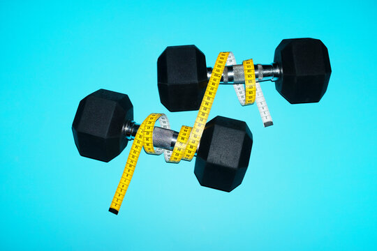 A tape measure wraps around dumbbells on a blue background