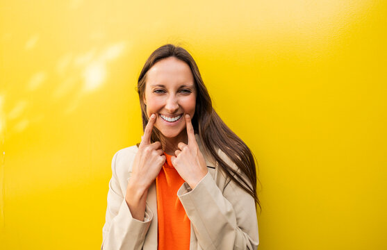 Smiling woman gesturing towards her mouth against yellow background