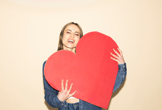 Smiling woman holding a large red paper heart showing love