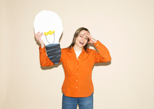 Smiling woman while holding a large paper light bulb and having an idea