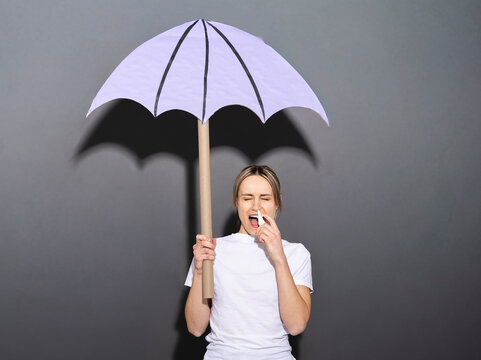 Woman using nasal spray under purple umbrella against cold