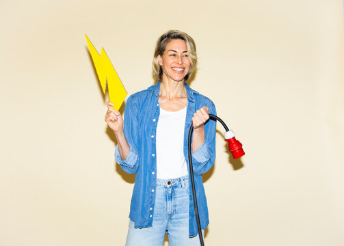 Smiling woman holds a charging cable and lightning bolt indoors