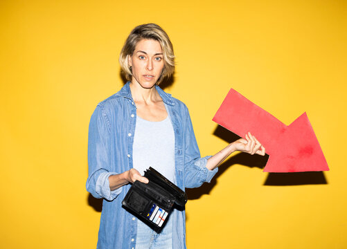 Worried woman holds wallet and red arrow showing inflation indoors