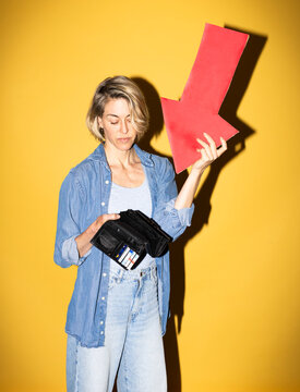 Mature woman holds red arrow pointing down at her open wallet
