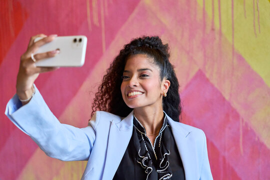 Smiling woman takes a smartphone selfie against a colorful wall