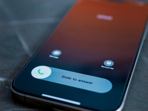 A close up view of a smartphone showing an incoming call. The screen displays options to swipe for answering or to decline the call.