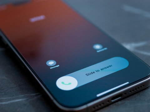 A close up of a smartphone display shows an incoming call. The options to slide to answer or decline the call are visible on the screen.
