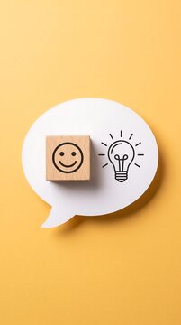 Wooden block with smiling emoticon icon and lightbulb sketch on speech bubble smiley face positive thinking problem solving thought process customer feedback