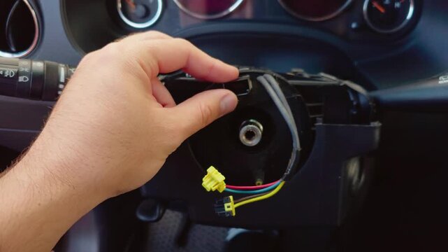 Clockspring inspection inside disassembled steering column during car repair. Technician hand rotating steering wheel clock spring near exposed wiring. Automotive electronics maintenance with airbag