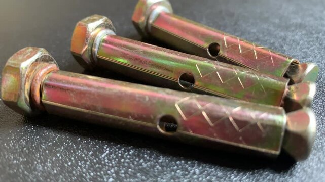 Real-time zoom out camera movement showing three yellow zinc plated sleeve anchor expansion bolts on a dark textured background. High angle macro close up 4K video for concrete fixing and masonry.