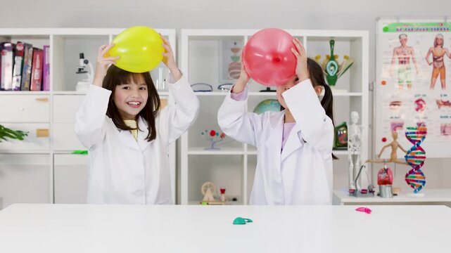 Two Schoolgirls in Lab Coats Rubbing Balloons on Their Hair for Science Experiment