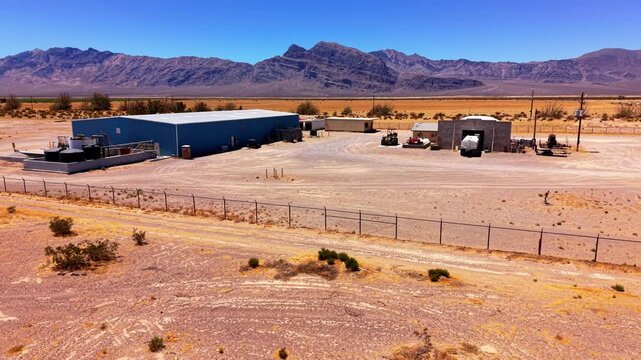 Smooth lateral drone movement follows a long blue industrial building and secure yard against a dramatic desert mountain range.