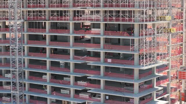 Smooth drone movement travels across the exposed concrete facade and dense scaffolding of a multistory building under construction.