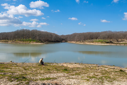 stanbul's Kazandere Dam. A person is fishing by the edge of a tranquil lake or reservoir. A vast, calm body of water stretches out right before the shore.