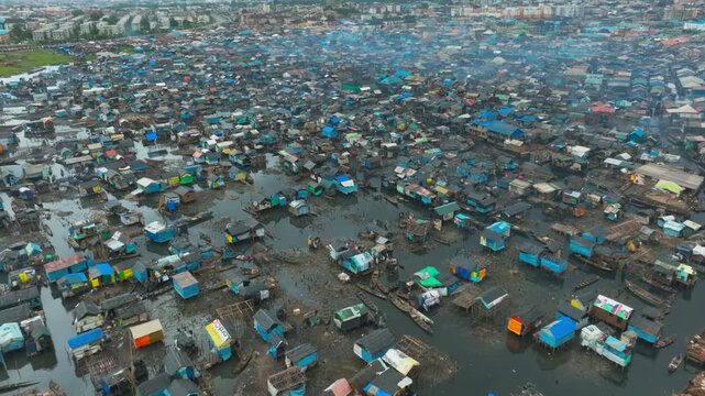 Aerial drone footage of Makoko Floating Village in Lagos, Nigeria, showing waterfront homes, fishing boats, wooden stilt houses, and life along the Lagos Lagoon