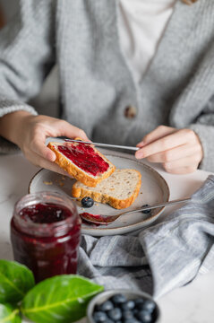 A woman's hands spread berry jam on toast during breakfast.