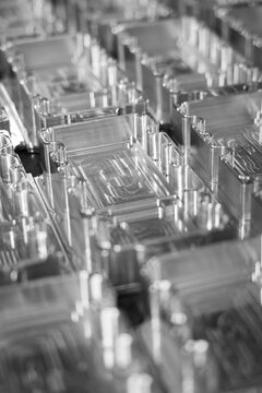 Macro close-up of precision CNC machined aluminium components with intricate milled pockets and cylindrical pillars, black and white, shallow depth of field