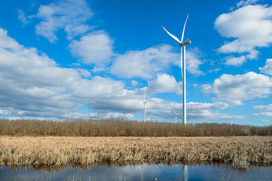 Wind turbines in Istanbul. Wind turbines are visible against a backdrop of a wetland area and a rural landscape. The sky is deep blue, with scattered white clouds