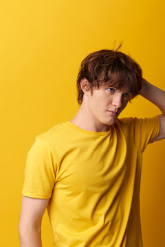 Young man in a yellow t-shirt touches the back of his head with downcast eyes, shy and uncertain. Studio shot on a yellow background. Concept of doubt or modesty.