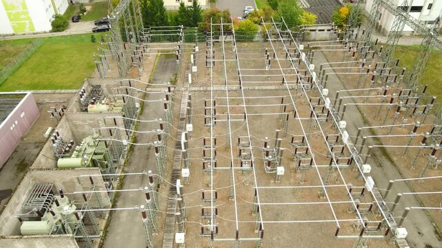 Aerial perspective of an electrical substation, showcasing the intricate grid of high voltage transmission lines, transformers, and industrial power generation infrastructure in an urban setting