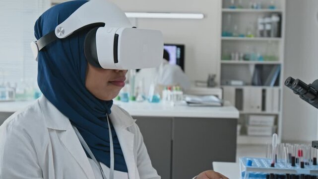 Young adult Asian woman scientist wearing VR headset operating handheld controller in laboratory. Clip suits biotechnology marketing and virtual medical training projects