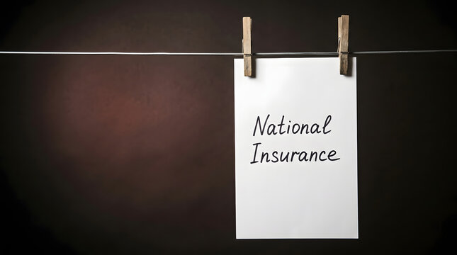 A single rectangular piece of white paper hanging from a horizontal wire by two wooden clothespins against a dark textured studio background with the words National Insurance written in black script