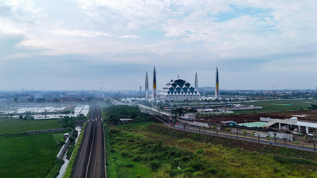 Aerial view of Al Jabbar Grand Mosque with surrounding green fields and railway tracks in Bandung, West Java, Indonesia.